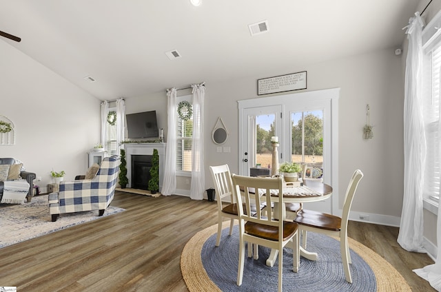 dining area featuring wood finished floors, visible vents, baseboards, lofted ceiling, and a fireplace with flush hearth