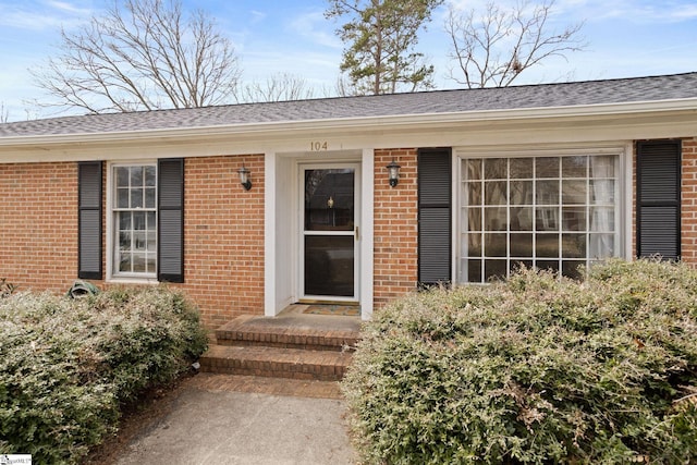 doorway to property featuring brick siding and a shingled roof