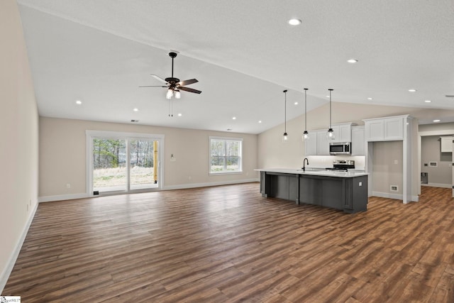 kitchen with a sink, vaulted ceiling, white cabinets, appliances with stainless steel finishes, and open floor plan