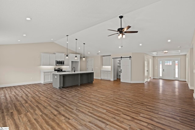 kitchen with a kitchen island with sink, white cabinets, appliances with stainless steel finishes, a barn door, and open floor plan