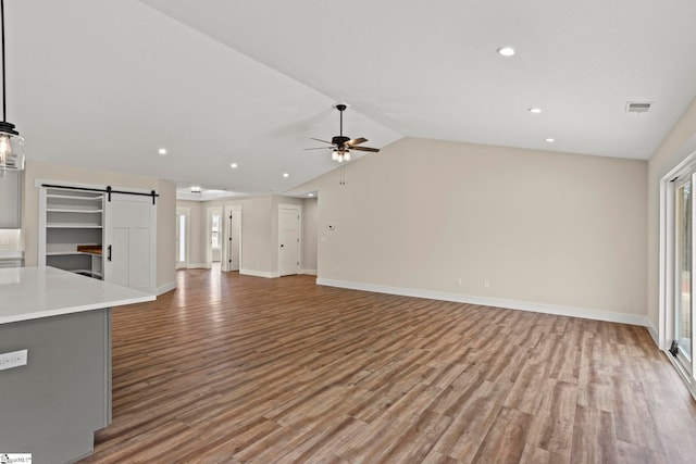 unfurnished living room with wood finished floors, visible vents, lofted ceiling, ceiling fan, and a barn door