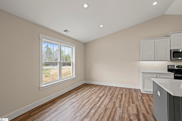 kitchen featuring appliances with stainless steel finishes, light countertops, lofted ceiling, and wood finished floors