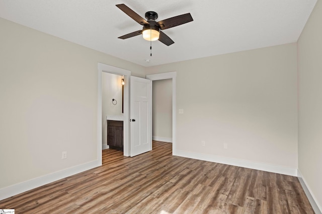 unfurnished bedroom with ceiling fan, baseboards, wood finished floors, and ensuite bathroom