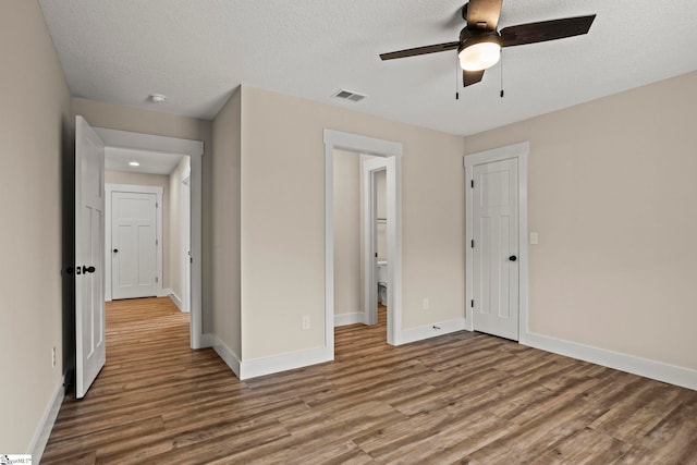 unfurnished bedroom with visible vents, a textured ceiling, baseboards, and wood finished floors