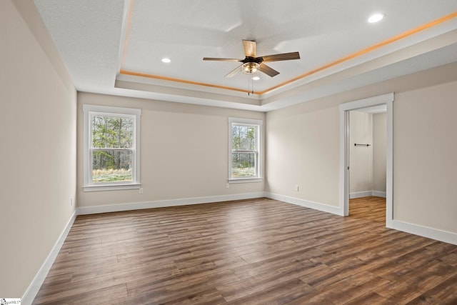 unfurnished room featuring baseboards, a raised ceiling, and dark wood-type flooring