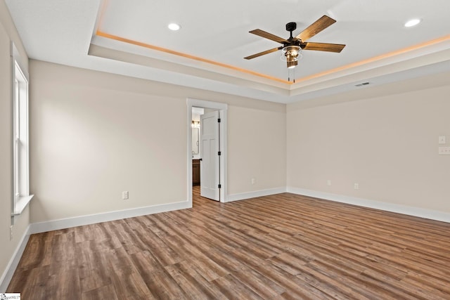 empty room featuring visible vents, baseboards, a tray ceiling, recessed lighting, and wood finished floors