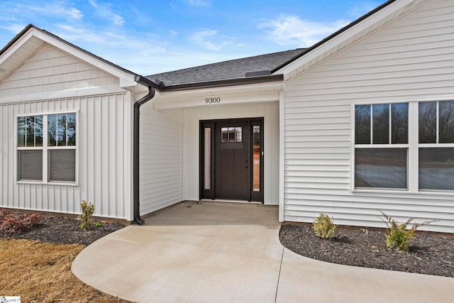 view of exterior entry with roof with shingles, board and batten siding, and concrete driveway