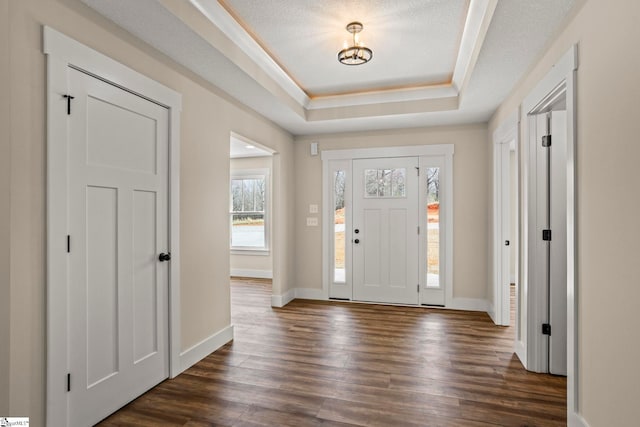 foyer entrance with a textured ceiling, baseboards, a raised ceiling, and dark wood-type flooring