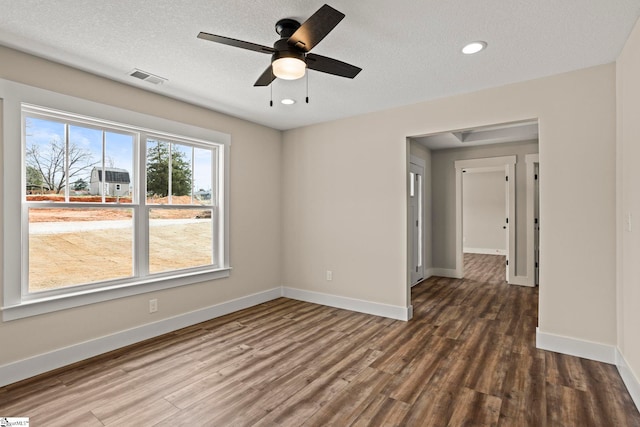 unfurnished room with a textured ceiling, wood finished floors, visible vents, and baseboards