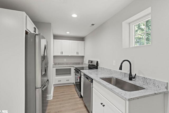 kitchen with light wood-type flooring, a sink, light stone counters, white cabinetry, and appliances with stainless steel finishes