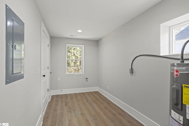 laundry room with visible vents, electric panel, wood finished floors, water heater, and baseboards