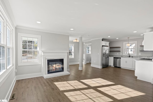 unfurnished living room with visible vents, dark wood finished floors, a sink, ornamental molding, and a glass covered fireplace