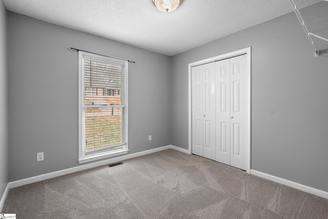 unfurnished bedroom with carpet, visible vents, baseboards, a closet, and a textured ceiling