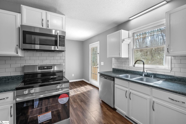 kitchen featuring dark wood-type flooring, a sink, dark countertops, stainless steel appliances, and white cabinets