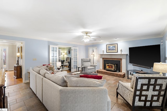 living room featuring a brick fireplace, ceiling fan, baseboards, ornamental molding, and stone tile flooring