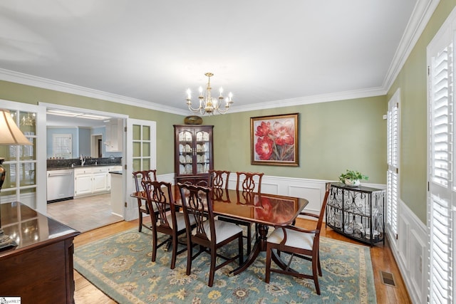 dining space with visible vents, light wood-style floors, an inviting chandelier, and crown molding