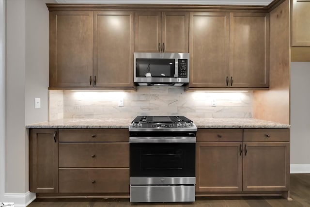 kitchen featuring light stone counters, stainless steel appliances, baseboards, and decorative backsplash