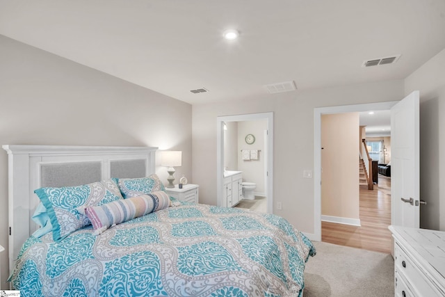 bedroom with visible vents, baseboards, light colored carpet, and ensuite bath