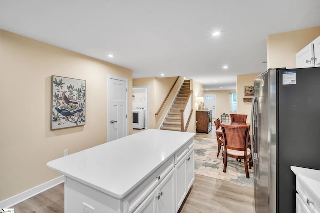 kitchen with washer / dryer, freestanding refrigerator, light countertops, light wood-type flooring, and a center island