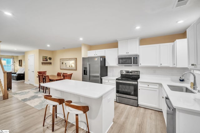 kitchen with visible vents, a kitchen island, appliances with stainless steel finishes, light wood-style floors, and a sink