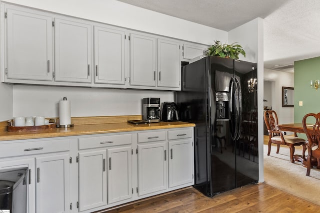 kitchen with black fridge with ice dispenser, wood finished floors, light countertops, and a textured ceiling