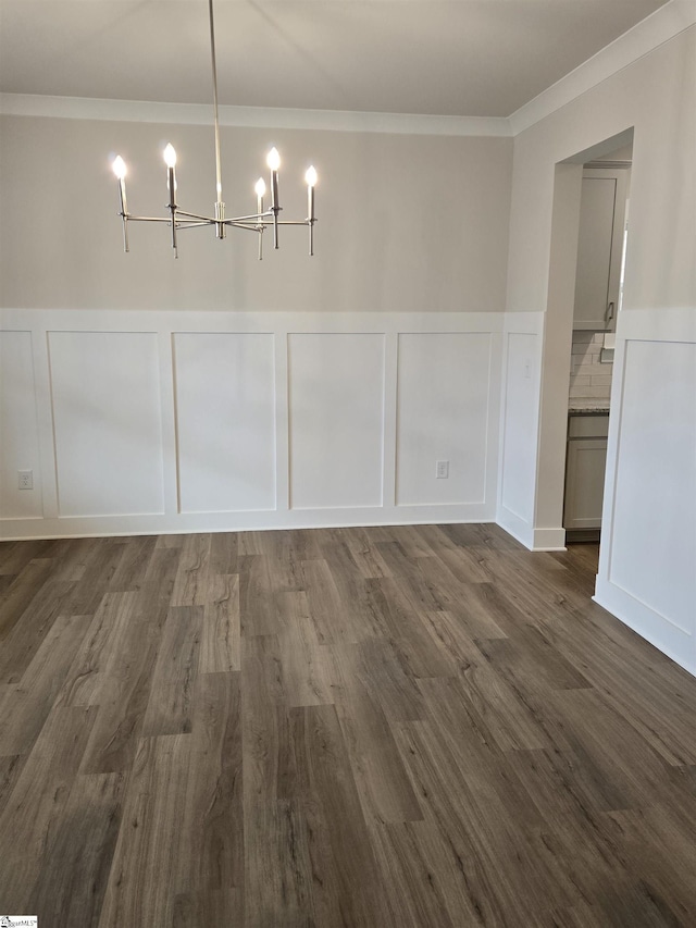 unfurnished dining area featuring an inviting chandelier, a decorative wall, dark wood-style flooring, and ornamental molding