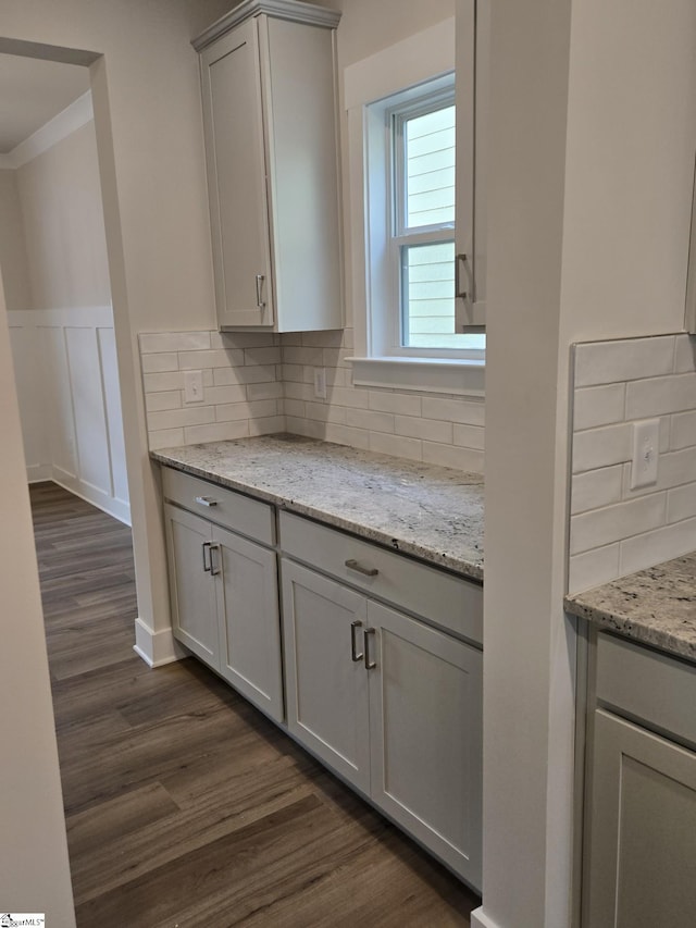 kitchen featuring a wainscoted wall, gray cabinetry, decorative backsplash, light stone countertops, and dark wood-style flooring