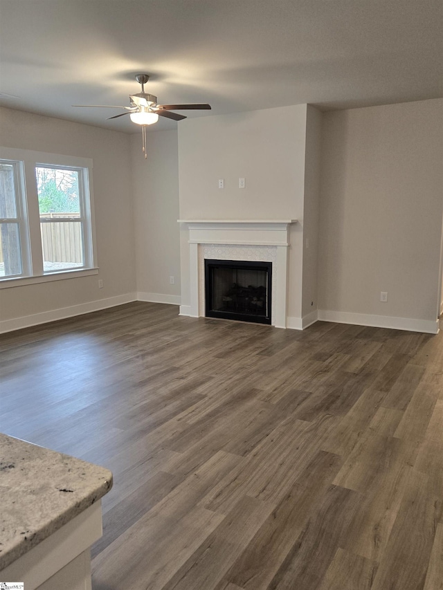 unfurnished living room with a ceiling fan, dark wood-style floors, a fireplace, and baseboards