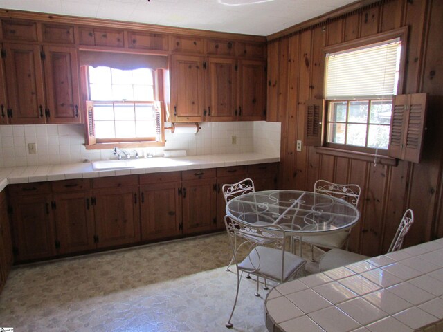 kitchen with backsplash, wood walls, light floors, brown cabinets, and a sink