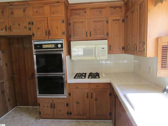 kitchen with brown cabinets, white appliances, tile countertops, and a sink