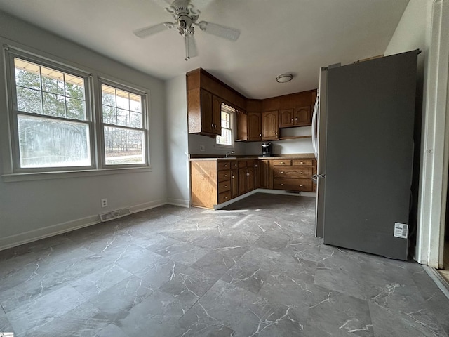 kitchen featuring visible vents, ceiling fan, baseboards, freestanding refrigerator, and a sink