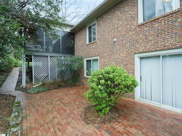 view of property exterior featuring a patio, brick siding, and a sunroom