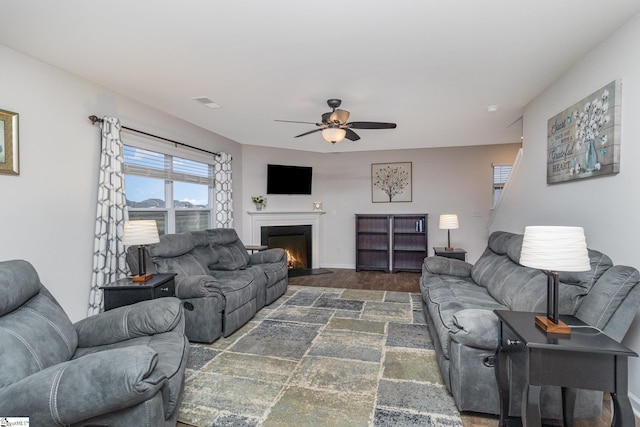 living area featuring visible vents, a fireplace with flush hearth, a ceiling fan, baseboards, and dark wood-style flooring