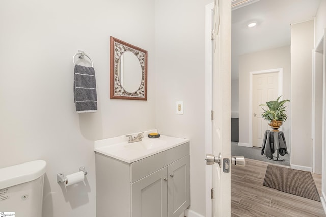 half bathroom with baseboards, toilet, wood finished floors, and vanity