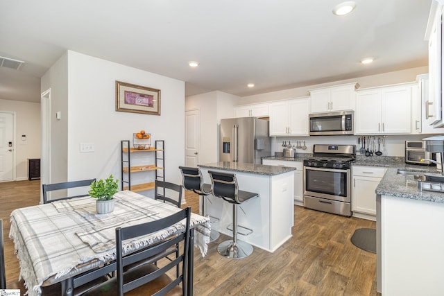 kitchen with dark wood-type flooring, a sink, a kitchen island, appliances with stainless steel finishes, and white cabinets