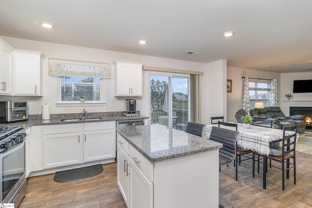 kitchen featuring visible vents, a sink, open floor plan, wood finished floors, and stainless steel range with gas stovetop