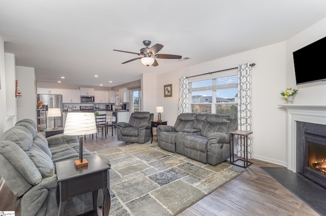 living room featuring visible vents, baseboards, recessed lighting, wood finished floors, and a glass covered fireplace