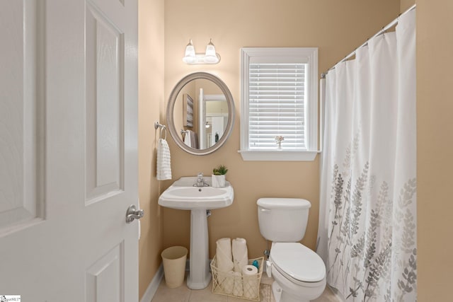 bathroom with a shower with curtain, toilet, a sink, tile patterned flooring, and baseboards