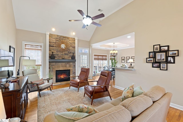 living room featuring visible vents, high vaulted ceiling, light wood-style floors, a stone fireplace, and baseboards