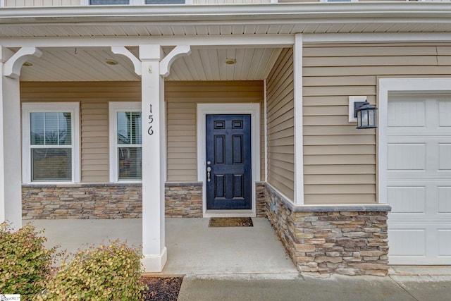 doorway to property with stone siding, covered porch, and a garage