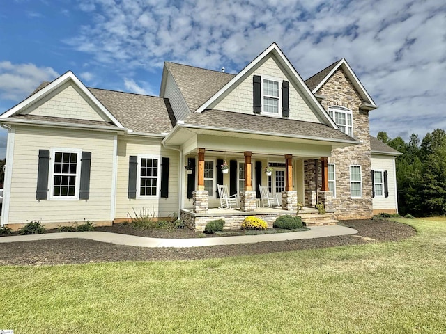 craftsman-style home with stone siding, a porch, a front yard, and roof with shingles