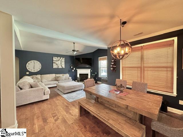 dining room featuring lofted ceiling, wood finished floors, a fireplace, and ceiling fan with notable chandelier