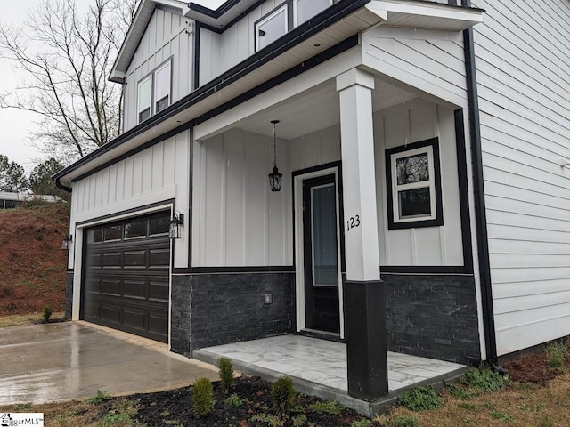 entrance to property featuring a garage, covered porch, board and batten siding, and stone siding