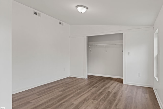 unfurnished bedroom with a closet, visible vents, lofted ceiling, and wood finished floors