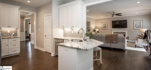 kitchen featuring a sink, stainless steel dishwasher, open floor plan, white cabinetry, and a peninsula