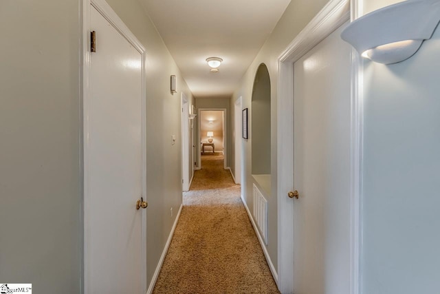 hallway with baseboards, visible vents, and light carpet