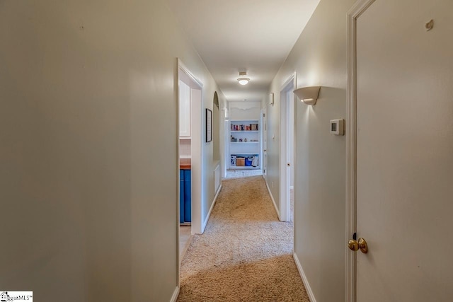 corridor with baseboards and light colored carpet