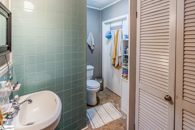 bathroom featuring a sink, a closet, crown molding, toilet, and tile walls