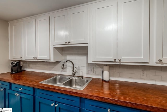 kitchen with butcher block countertops, blue cabinetry, white cabinets, and a sink