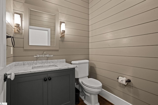 half bathroom featuring wood walls, toilet, and vanity